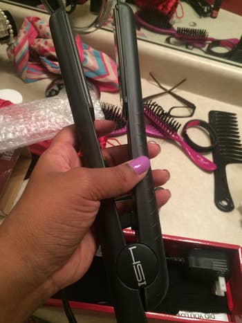 reviewer holding black straightener in hand with beauty products on counter
