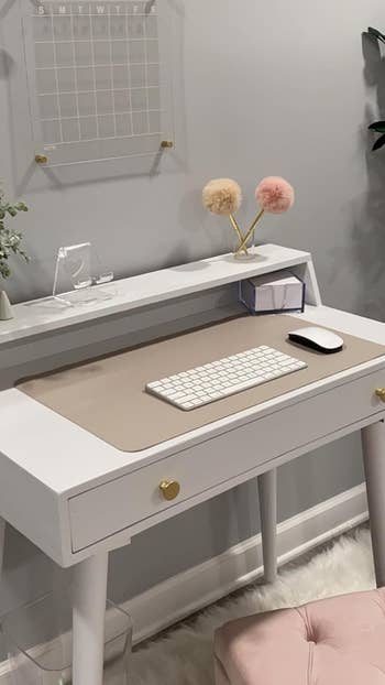 A sleek achromatic  table  with a tan mat, keyboard, mouse, and decorative items connected  top, including a calendar and 2  fluffy pom-poms successful  a solid  holder