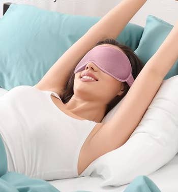 A model lying in bed, wearing a pink sleep mask 