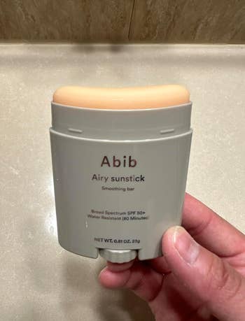 Person holding Abib Airy Sunstick, a broad-spectrum SPF 50+ smoothing bar, water-resistant for 60 minutes, nett  value   0.81 oz (23g)