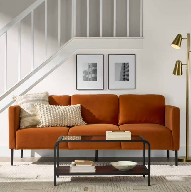 Modern surviving country with a sofa, pillows, 2 framed artworks, and a java table. A level lamp is beside the sofa nether a staircase