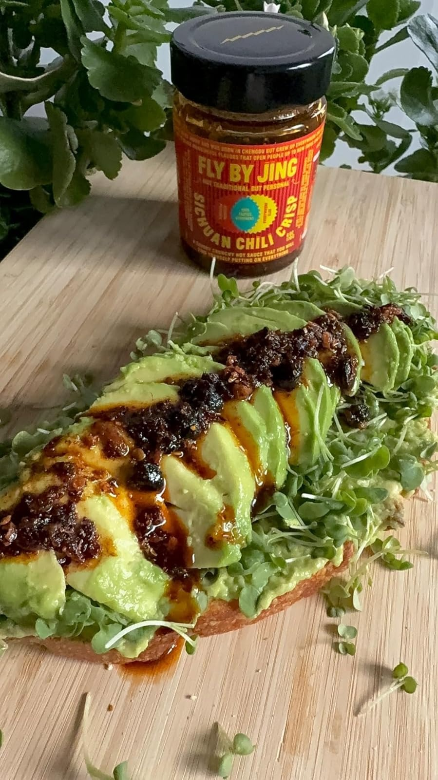 Avocado toast topped with microgreens and chili sauce, with a jar of 