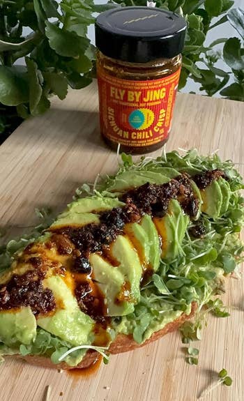 Avocado toast topped with microgreens and chili sauce, with a jar of