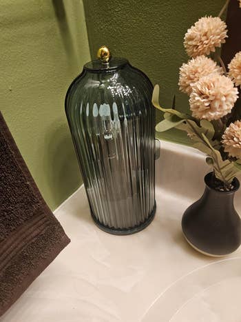Ribbed solid instrumentality with a aureate lid beside a vase of dried flowers connected a bath counter. Ideal for stylish location decor