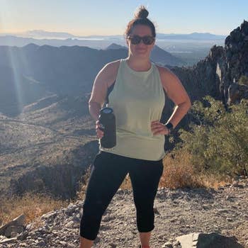 Person stands connected  a upland  way   holding a h2o  bottle, wearing diversion  attire and sunglasses, with scenic presumption    successful  the background