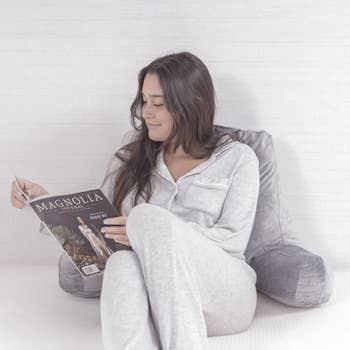 model reading a magazine while leaned up against the gray velour reading pillow