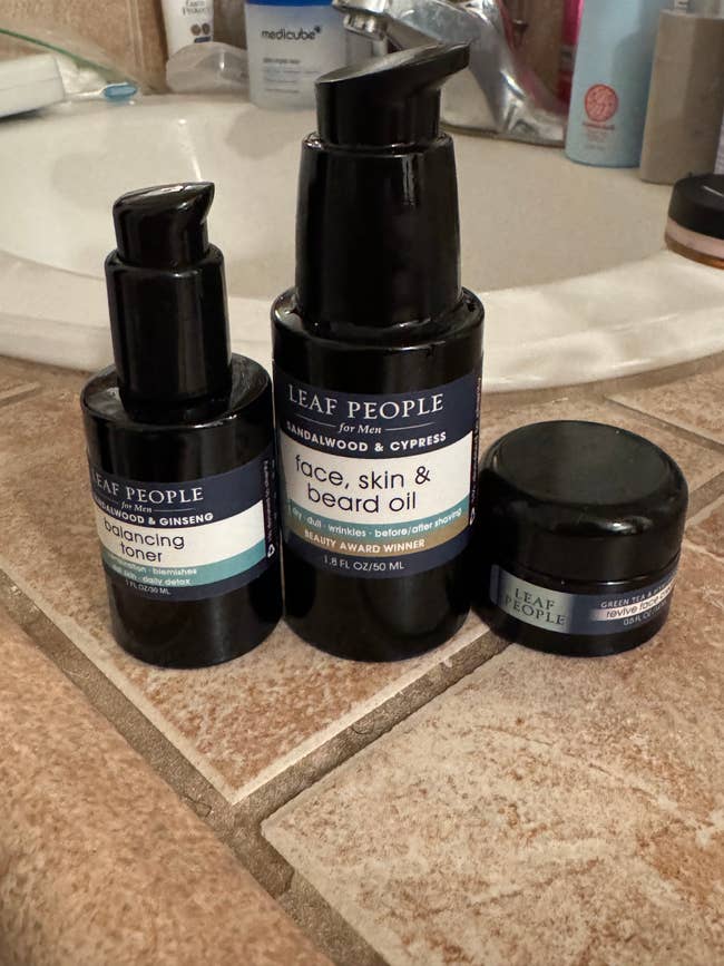 Skincare products on a bathroom counter, featuring toner, face, skin & beard oil, and rejuvenating lotion by Leaf People