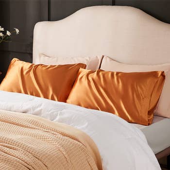 two pillows covered in orange satin pillowcases on a bed