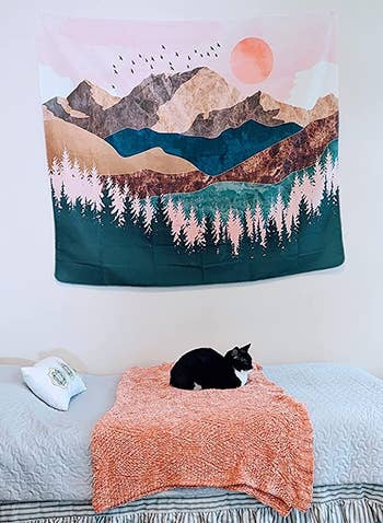 reviewer photo of the tapestry hanging above their cat laying on their bed