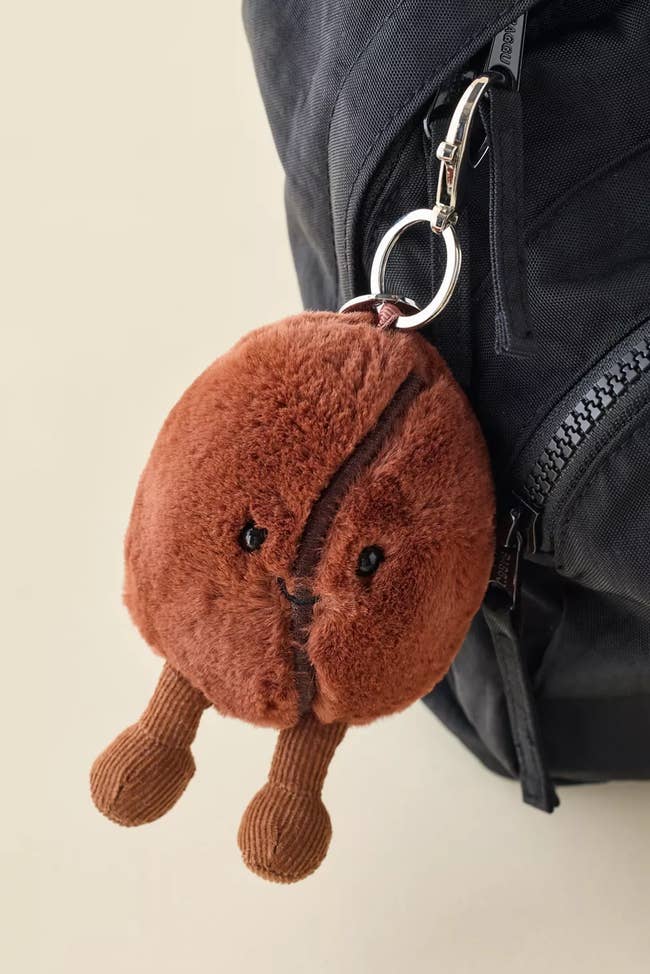 Plush java  legume  keychain with a zip pouch  and dangling feet attached to a backpack zipper