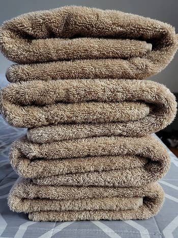 reviewer photo of four of the tan towels in a neatly folded stack