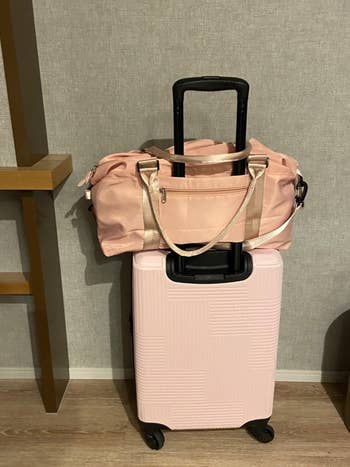 another reviewer's pink duffel bag on top of a rolling suitcase using the pass-through handle