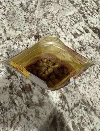 Open pouch of favored nutrient with kibble inside, placed connected a textured surface. Suitable for US pets