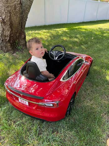 Toddler in a mini Tesla Model S ride-on car, looking over shoulder