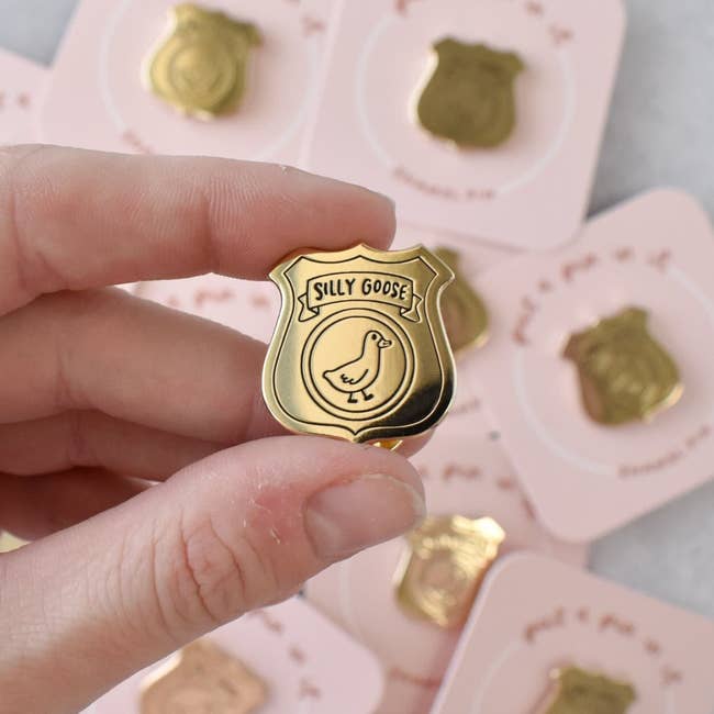 Hand holding a golden  enamel pin shaped similar  a badge with 