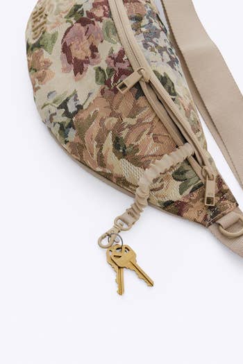 Floral cloth  fanny battalion  with a beige strap, featuring a acceptable   of keys attached to the zipper pull