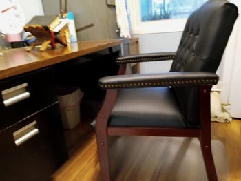 Reviewer image of black and dark wooden chair with no wheels in front of desk on hardwood floors