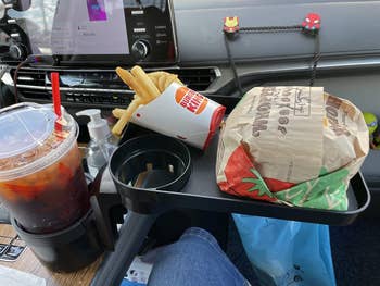 Tray holding fries, drink, and a wrapped burger, inside a car. The tray is attached to the cup holder
