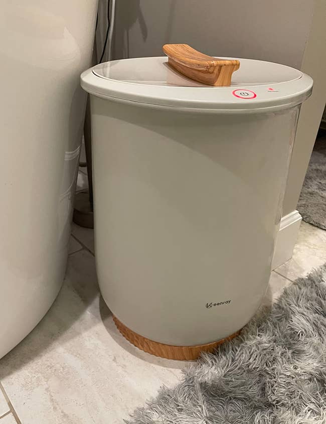 a reviewer photo of the towel warmer sitting on a bathroom floor 