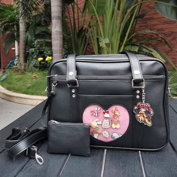 Black handbag with a small purse, featuring a pink heart-shaped front window displaying various character pins 