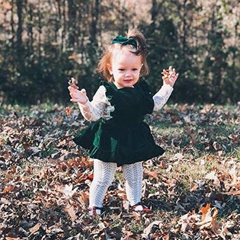 a toddler in a dark green velvet apron dress