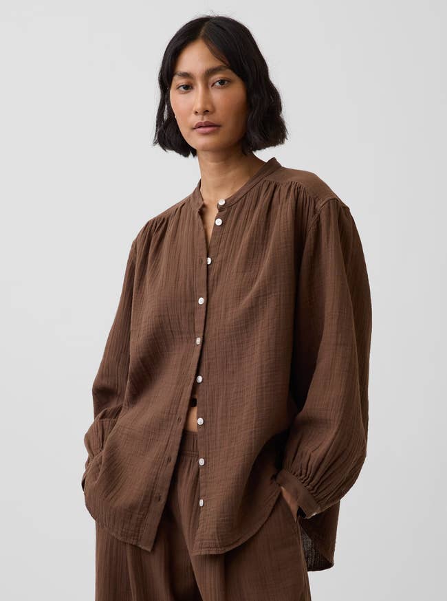 Person wearing a casual, loose-fitting button-up garment  and matching pants, hands successful  pockets, posing against a plain backdrop