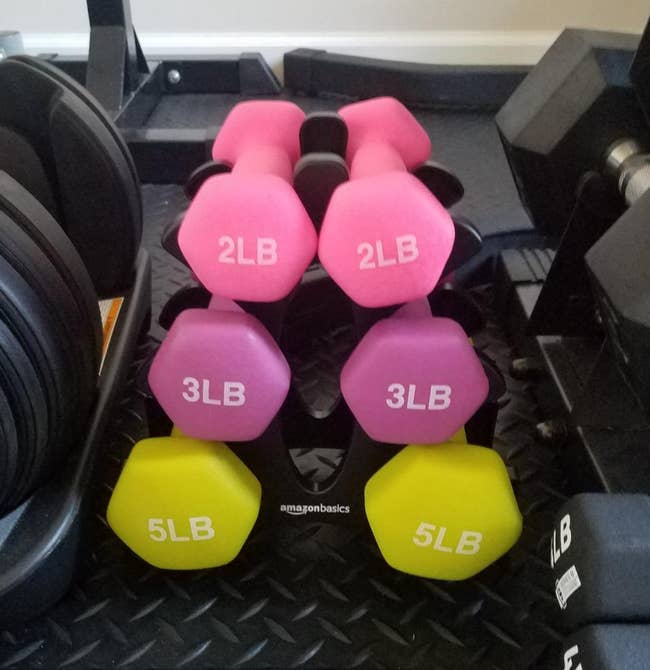 reviewer pic of set of pink 2-pound weights, dark pink 3-pound weights, and yellow 5-pound weights on black stand