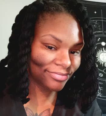 Person with braided hairstyle and a tattoo smiles slightly, with an astronomy-themed background. Image for shopping content