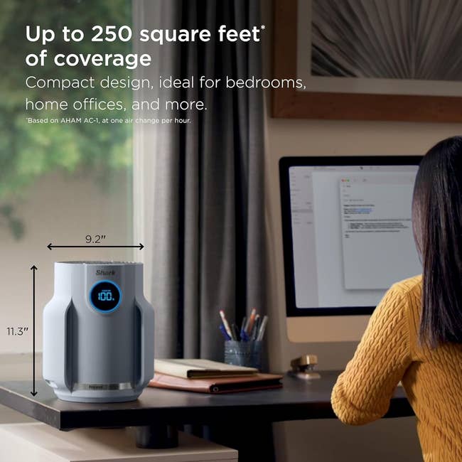 A idiosyncratic   sits astatine  a table  adjacent  to a compact aerial  purifier, highlighting its sum  of up   to 250 quadrate  feet, perfect  for location  offices and bedrooms