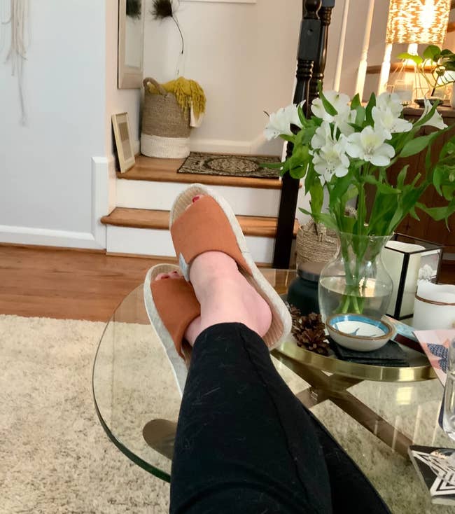 pic of reviewer wearing cushy open-toe orange house shoes while sitting on a couch