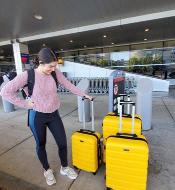 reviewer standing outside the airport next to three yellow rolling suitcases of varying sizes