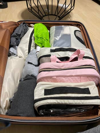Open suitcase with neatly packed apparel  and bags, including a pinkish  zippered organizer and compact umbrella. Suitable for a question   buying  article