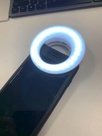 A smartphone with a circular LED selfie light attached, placed on a desk
