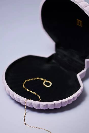 A shell-shaped jewelry box open with a gold necklace inside