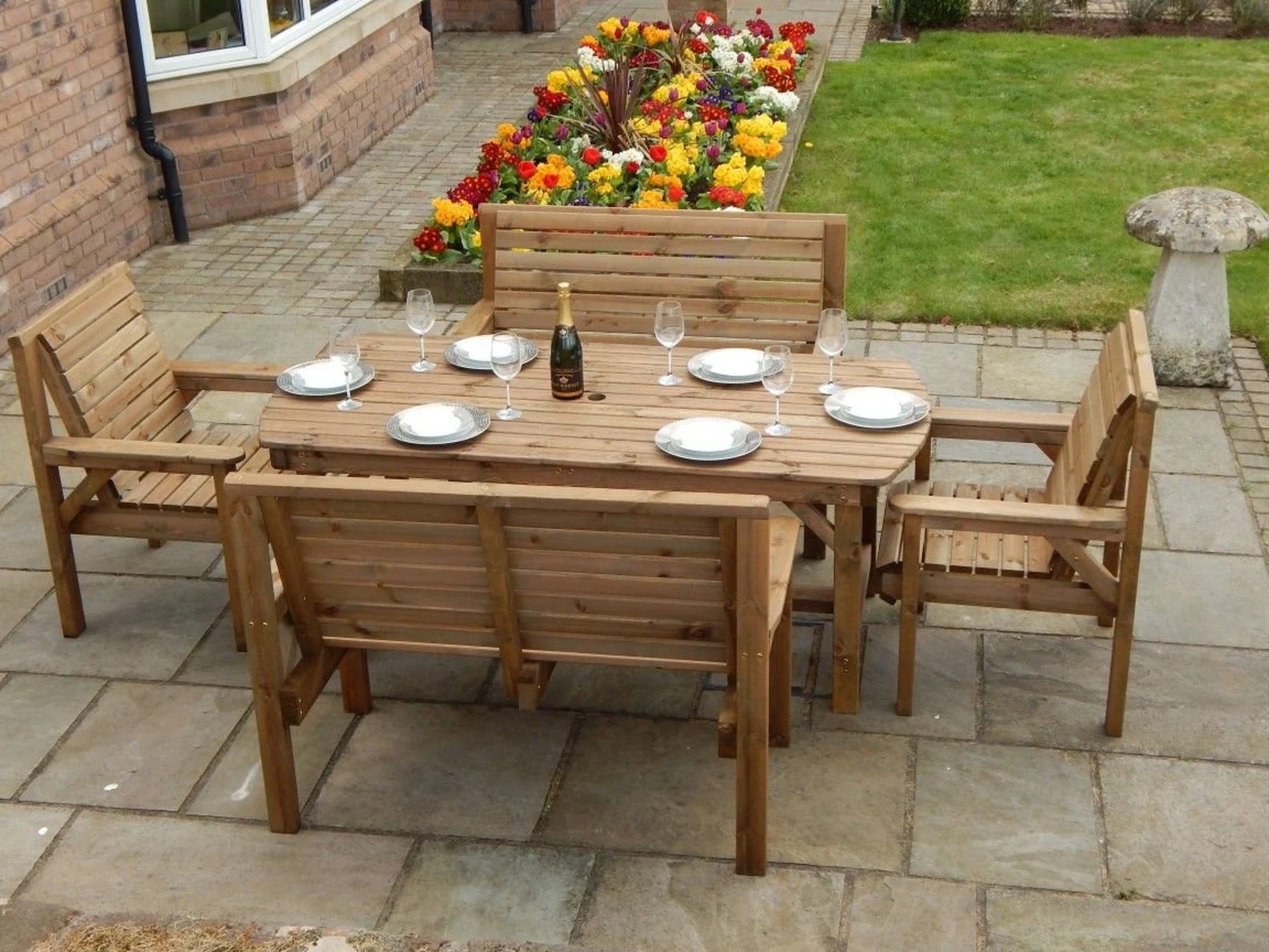 Light wooden table with plates and glasses surrounded by matching chairs and benches on a stone patio
