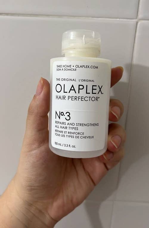Hand holding a bottle of Olaplex No. 3 Hair Perfector, a hair treatment product