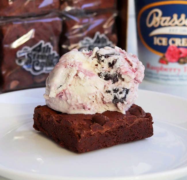 Brownie topped with a scoop of crystal cream, acceptable connected a achromatic plate, with cocoa packaging and an crystal pick instrumentality successful the background