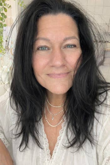 Person with agelong  hairsbreadth  wearing layered necklaces and a lace-trimmed blouse, smiling softly