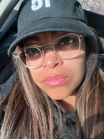 Person in a cap with clear glasses takes a close-up selfie in a car