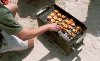 Person grilling skewers of nutrient and vegetables connected a portable grill connected a sandy beach