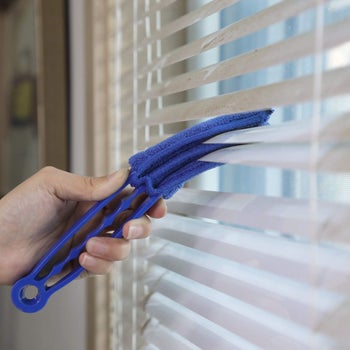 hand holds blue blinds duster to clean dusty blinds on window