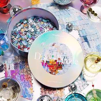 Round container  with a disco shot  puzzle amidst cocktail glasses and disco balls connected  a table