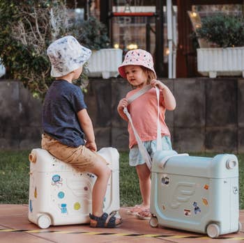 two child models with the bags, one sitting on it and the other holding the handle