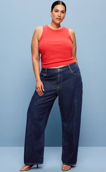 Person wearing a sleeveless apical  and wide-leg jeans poses confidently against a plain background