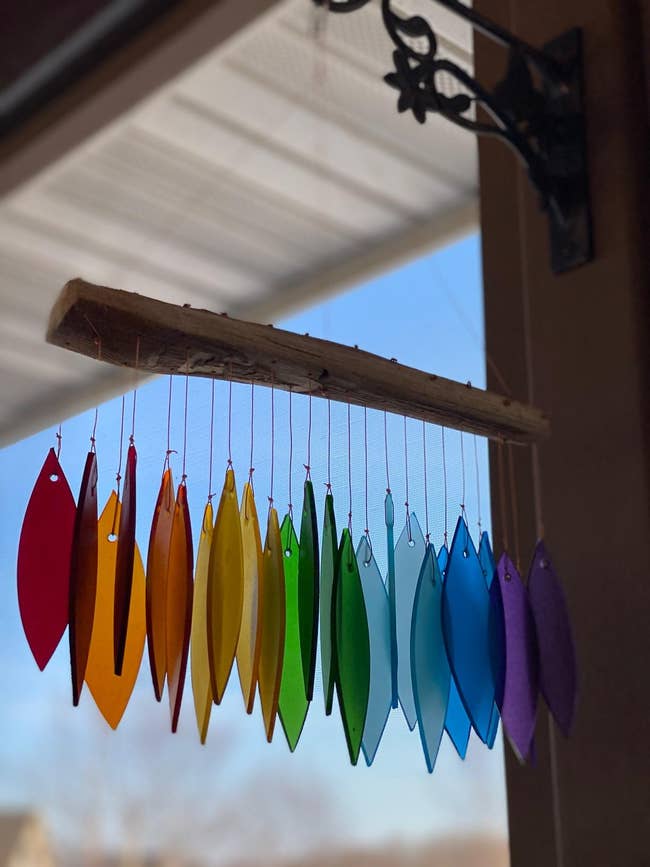 Hanging glass suncatchers in various shapes and primary colors against a clear window with visible sky