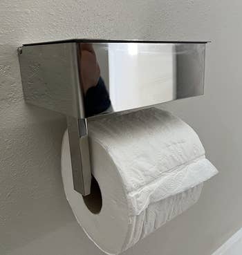 A reviewer's stainless steel toilet paper roll holder with a flip top lid compartment on top 