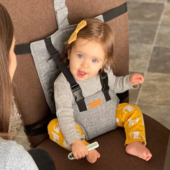 a child sitting on a regular chair strapped into the harness