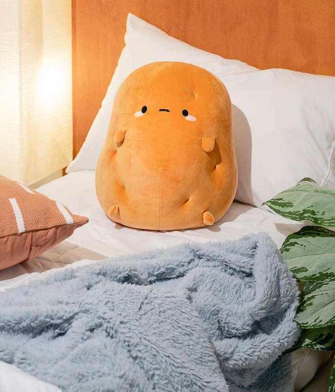 large plush potato with a face and short arms and legs sitting on a bed