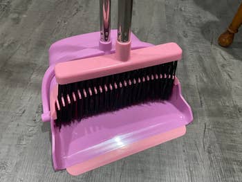 A broom and dustpan acceptable   with upright handles and achromatic  bristles, resting connected  a tiled floor