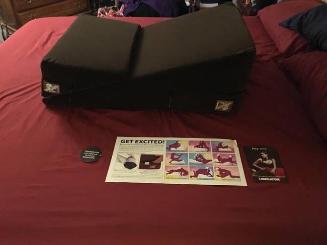 Black wedge and ramp sex pillow on red sheets with instructions